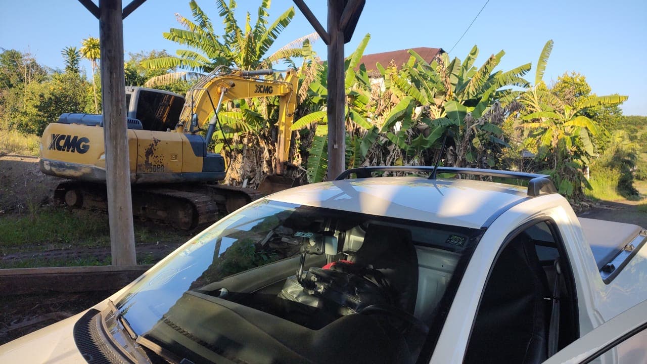 Escavadeira de esteiras em área rural, com a caminhonete de apoio em primeiro plano