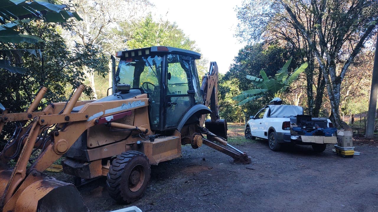 Retroescavadeira parada em área rural, com a caminhonete de apoio ao fundo